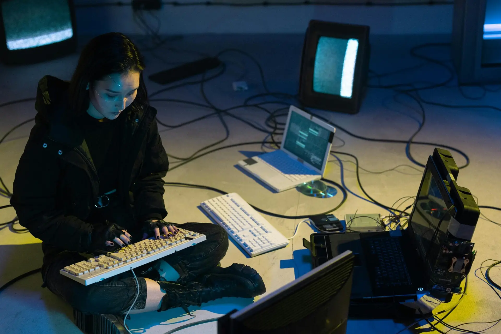 Young Asian woman engaged in computer hacking in a dimly lit, technologically equipped room.